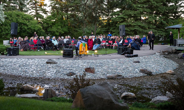 A group of people listening to a jazz player in the Japanese gardens in Lethbridge. 