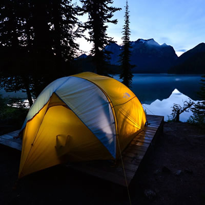 Picture of tent set up on lakeshore with mountains in the background. 
