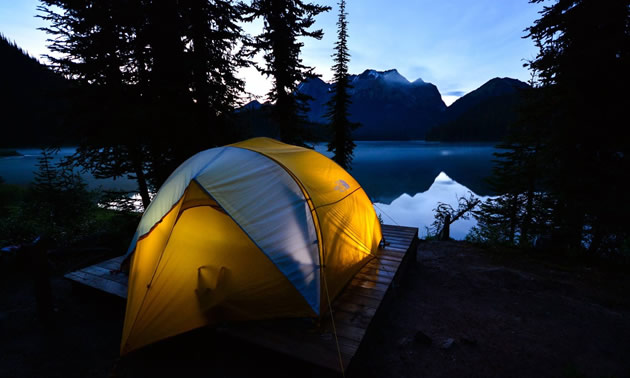 Picture of tent set up on lakeshore with mountains in the background. 