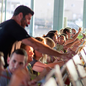 A group of students painting while a teacher is shown giving individual instruction to one of the students. 