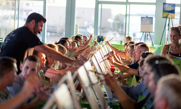 A group of students painting while a teacher is shown giving individual instruction to one of the students. 