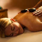 A bare-shouldered woman lying down receiving a hot stone massage