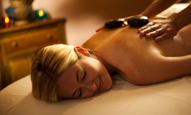 A bare-shouldered woman lying down receiving a hot stone massage