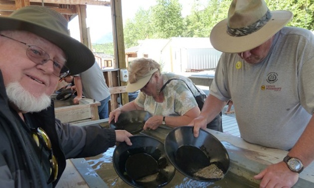 children, adults and a costumed interpreter panning for gold at a long trough filled with water