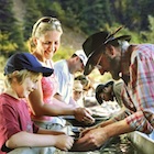 children, adults and a costumed interpreter panning for gold at a long trough filled with water