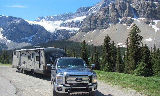 The Rogoza family's RV and truck on a road with snowcapped mountains in the background.