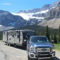 The Rogoza family's RV and truck on a road with snowcapped mountains in the background.