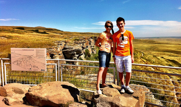 Two people stand on a cliff at the Head-Smashed-In-Buffalo Jump Interpretative Centre. The backdrop is a stunning prairie view over one of the world's oldest, largest and best-preserved buffalo jumps.