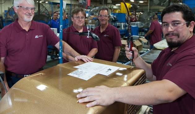 RV Products associates who had a hand in manufacturing the unit are shown with the gold guilded air conditioning unitl in the factory.