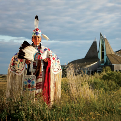 A First Nations woman in traditional garb stands outside the Wanuskewin Heritage Park. 