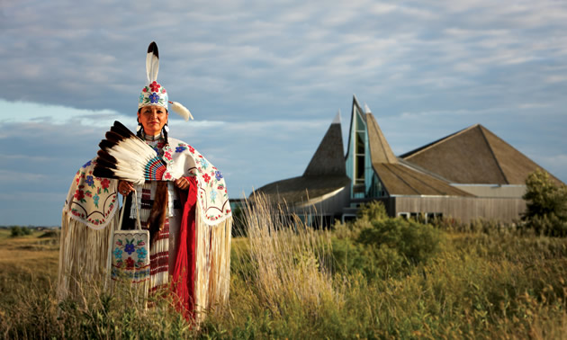 A First Nations woman in traditional garb stands outside the Wanuskewin Heritage Park. 