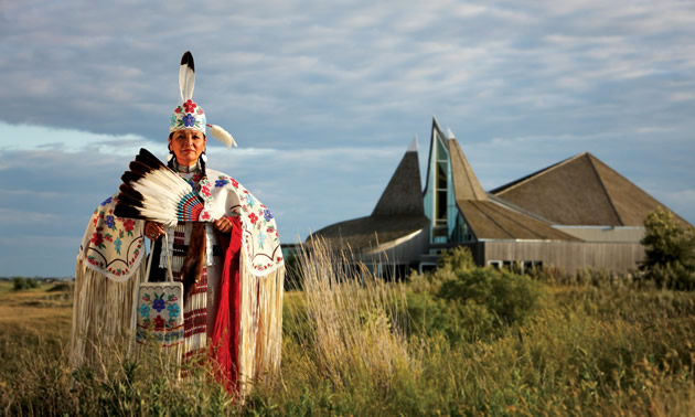 A First Nations woman in traditional garb stands outside the Wanuskewin Heritage Park.