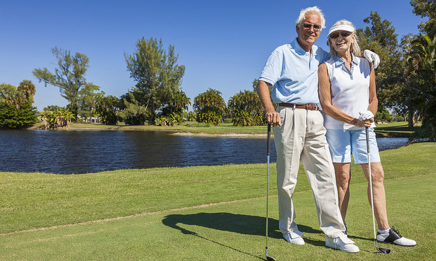 A happy senior couple standing with their clubs on a golf green. 
