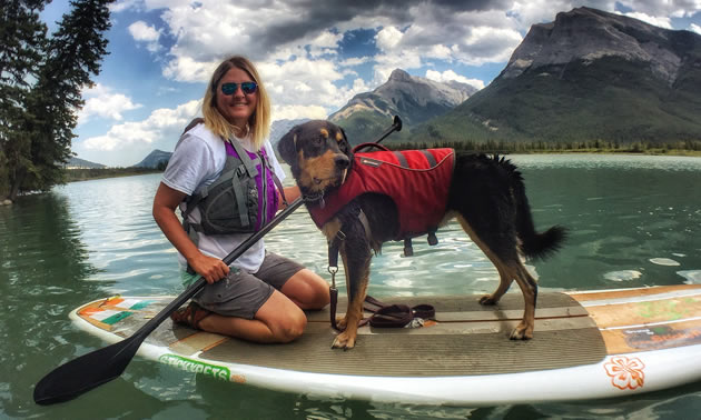 Christine Newmanis kneeling on a paddleboard with a shelter dog, Vincent (a Rottweiler-hound mix).