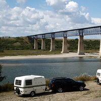 Campers parked by the river looking out toward the SkyTrail Bridge. 