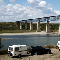 Campers parked by the river looking out toward the SkyTrail Bridge.