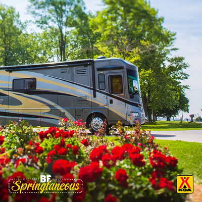 Picture of fifth wheel with red flowers in foreground. 