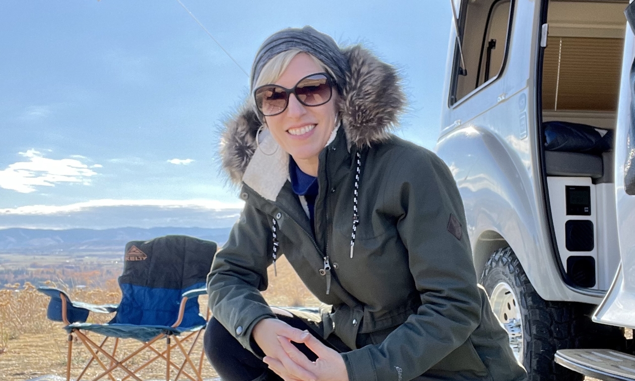 Tara Burnett kneeling down in front of her RV with a beach in the background