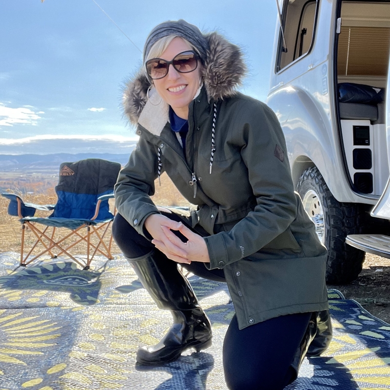 Tara Burnett kneeling down in front of her RV with a beach in the background