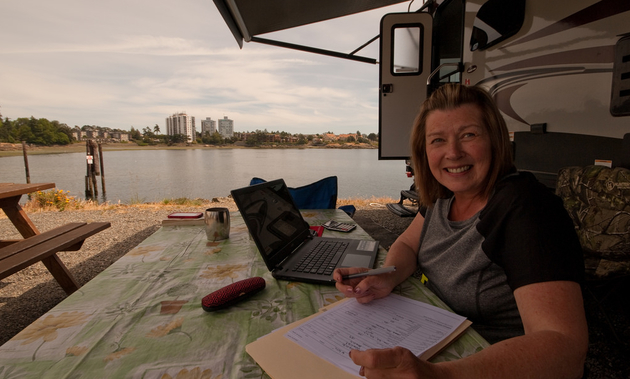 Working remotely takes a bit of planning. Here, a woman sits at a picnic table with a laptop and paperwork outside her RV. 