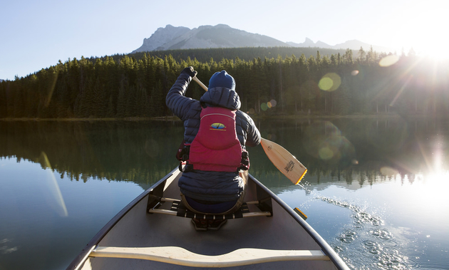 Person paddling a canoe by the mountains