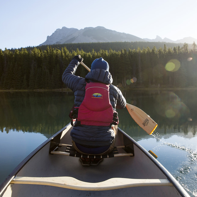 Person paddling a canoe by the mountains