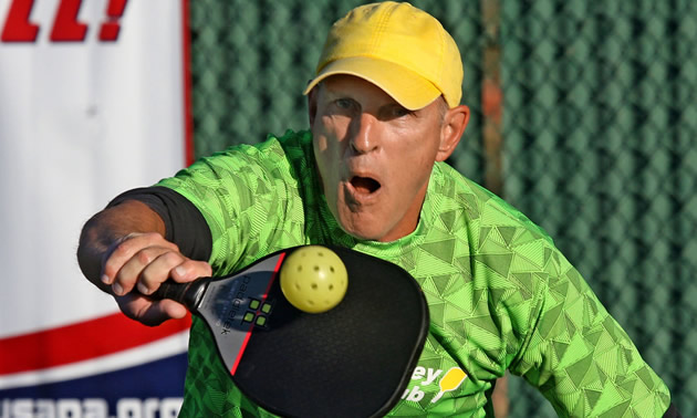 Pickleball player wearing yellow ball cap.