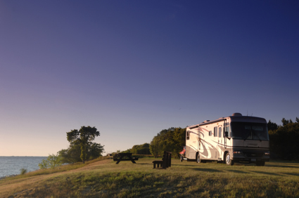 A man stands beside his RV and looks at the view of a lake.