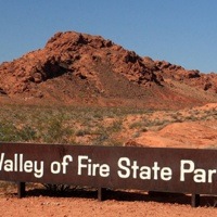 A photo of the Valley of Fire State Park sign with a red mountain in the background.