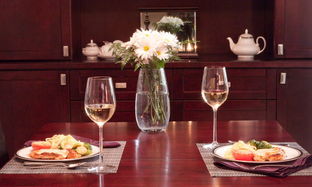 Two dinner place settings with wine glasses and white flowers are set on a wooden table.