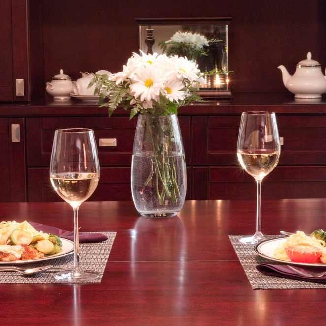 Two dinner place settings with wine glasses and white flowers are set on a wooden table.