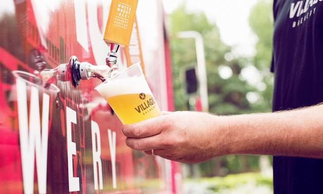 A man is filling a glass of beer from a beer tap at the Village Brewery.