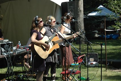 three women perform with guitars outdoors