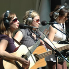 three women perform with guitars outdoors