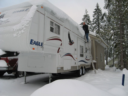 A man sweeps snow from the roof of an RV