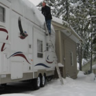 A man sweeps snow from the roof of an RV