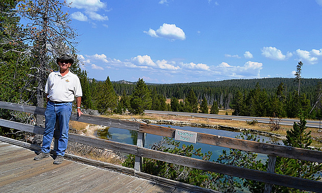 man standing on a bridge near a riverbank